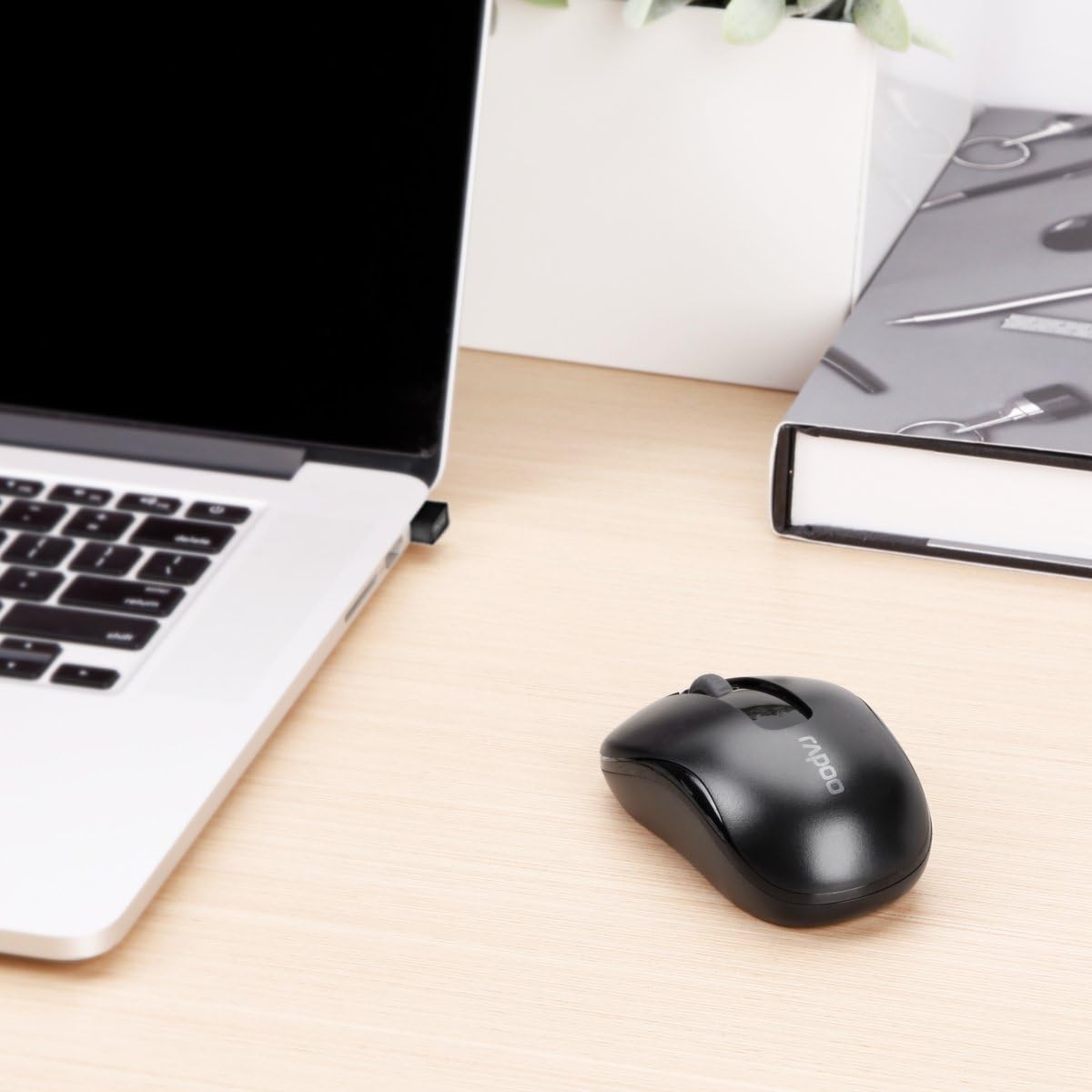 Black computer mouse on a desk next to a laptop and a notebook.